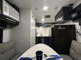 Inside a modern rv rental: dining table setup, compact kitchen, AC unit, and entertainment for a comfortable journey.