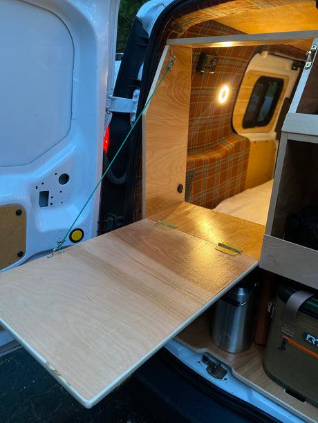 RV rental's custom camper van interior features a fold-down table with storage. Plaid walls & lights create a cozy space.
