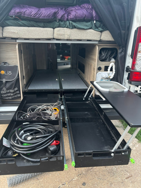 View inside an RV rental's rear: organized pull-out storage drawers, a portable sink, and bed above.