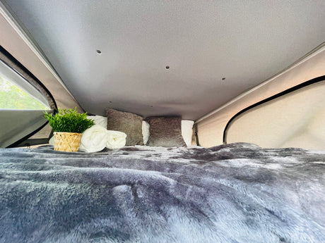 Cozy bed with plush blanket, pillows, and plant inside an RV rental pop-top sleeping area.