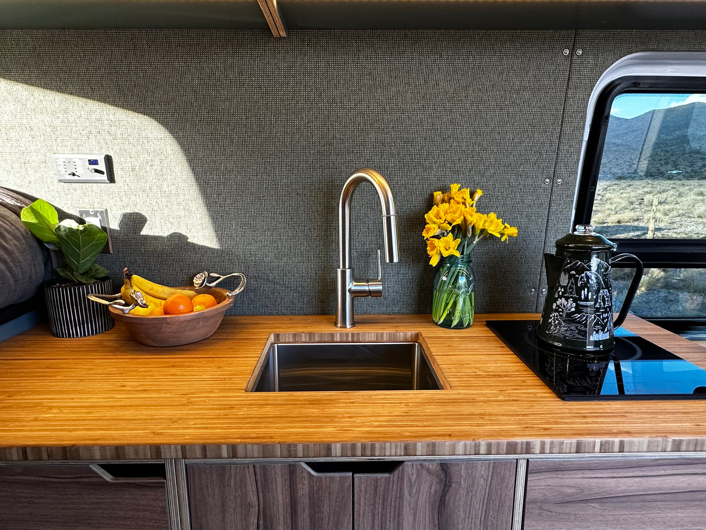 Inside an RV rental: functional kitchen featuring a wood counter, sink, induction cooktop, and mountain views.