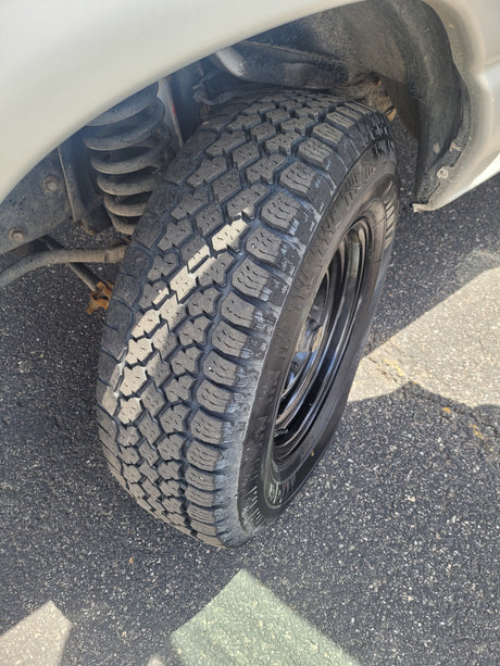 Front wheel of an RV rental, featuring a rugged all-terrain tire and visible coil spring suspension components.