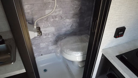 Compact RV rental interior featuring a wet bath with toilet/shower combo, sink, and control panel. Efficient space usage.