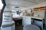 This RV rental interior features a bed, kitchen with sink & fridge, and a cozy seating area, offering scenic views.