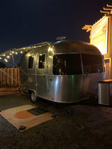 A stylish Airstream trailer, set up as an RV rental, glows with string lights at night at Marina Dunes campground.