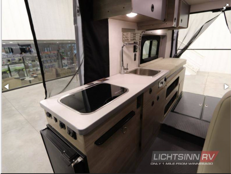 Step inside this RV rental! A compact interior boasts a full kitchen with sink/stovetop, fridge, & versatile living/sleeping zone.