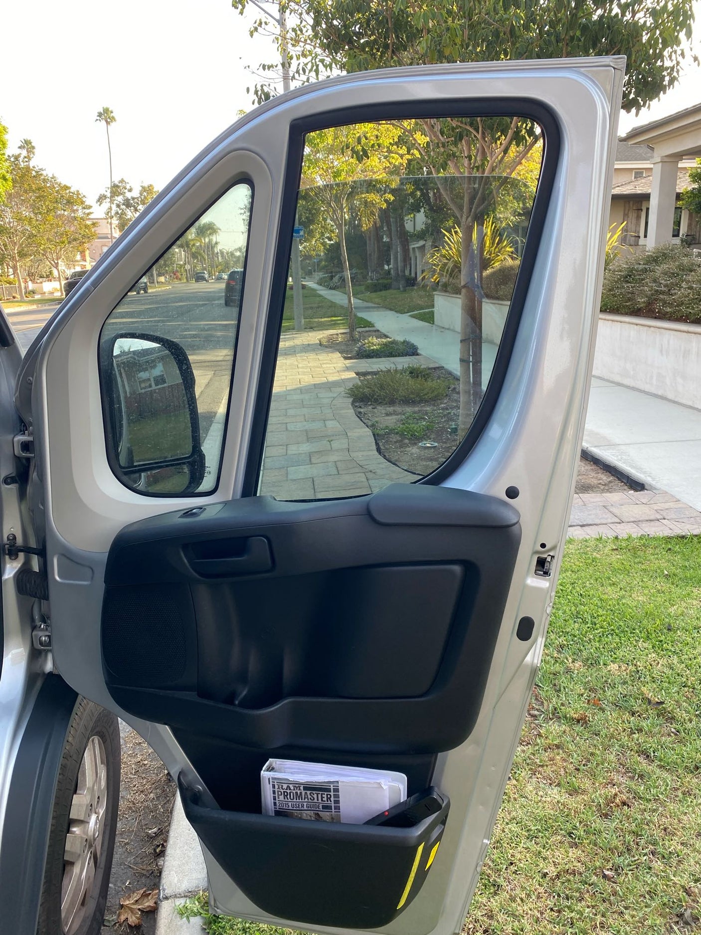 Open driver's door of a Ram ProMaster camper van, with interior storage and street view. Ideal for your next RV rental trip.