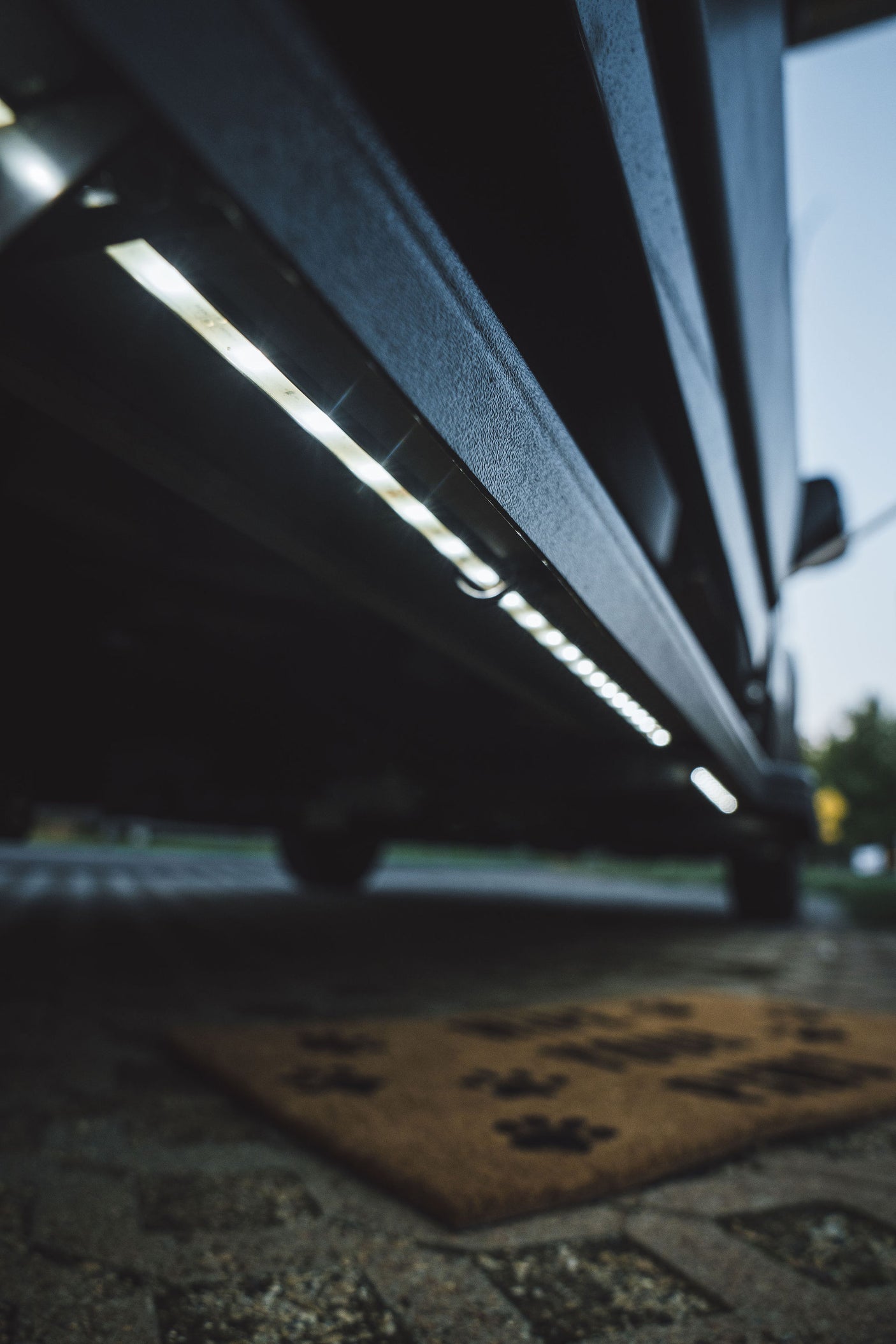 Bright LED exterior lighting on an RV rental, illuminating the ground and a paw-print doormat for easy entry at night.