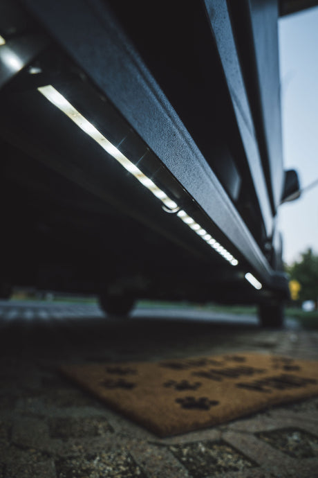 Bright LED exterior lighting on an RV rental, illuminating the ground and a paw-print doormat for easy entry at night.