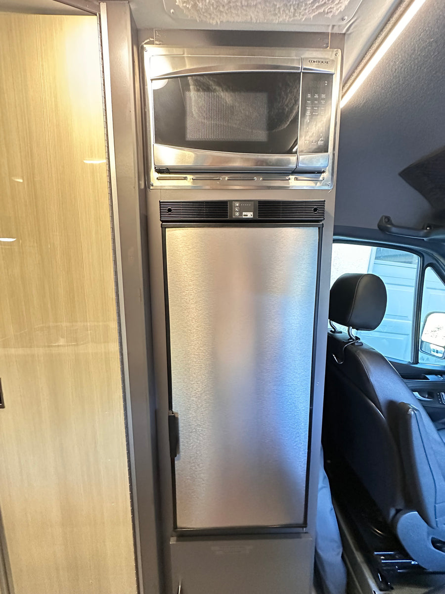 RV rental interior features a compact, stacked stainless steel microwave and refrigerator/freezer, perfect for mobile living.