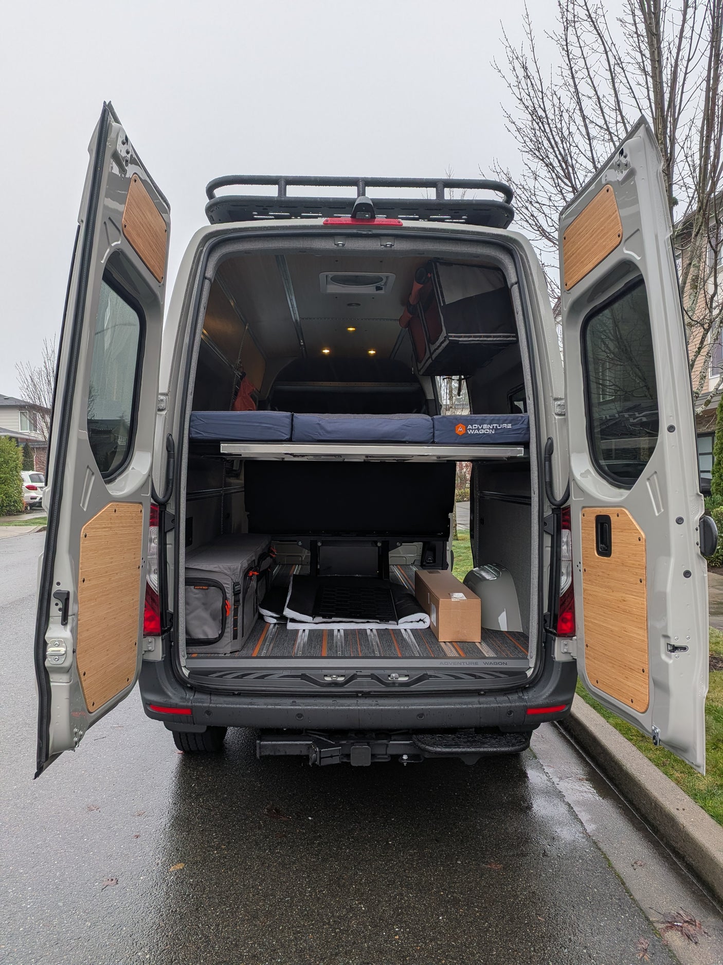 This custom camper van conversion is ideal for RV rental adventures, featuring an open rear with bed, storage, and roof rack.