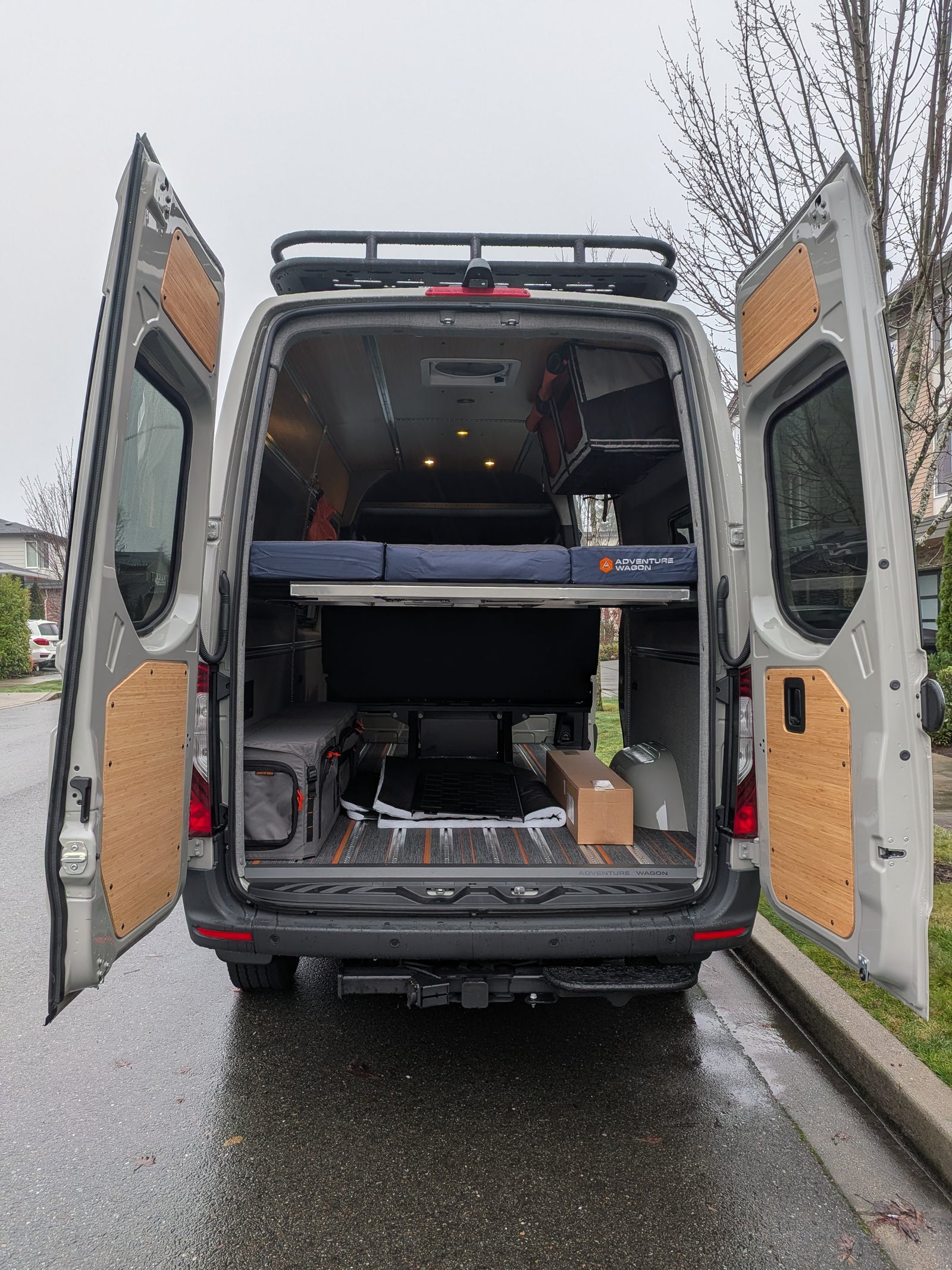 This custom camper van conversion is ideal for RV rental adventures, featuring an open rear with bed, storage, and roof rack.