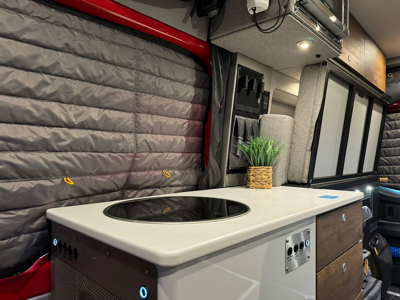 Modern RV rental interior: compact kitchen with cooktop, storage, and insulated windows for comfortable travels.
