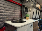 Modern RV rental interior: compact kitchen with cooktop, storage, and insulated windows for comfortable travels.