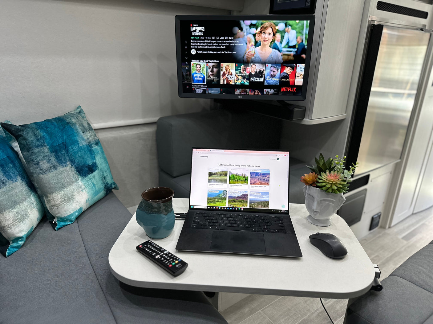 Cozy RV rental interior with a TV showing Netflix, a laptop browsing national parks, and comfortable seating.