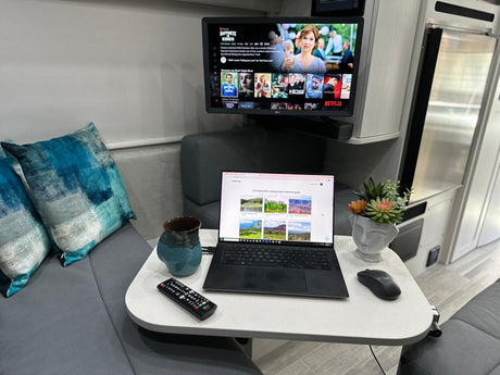 Cozy RV rental interior with a TV showing Netflix, a laptop browsing national parks, and comfortable seating.