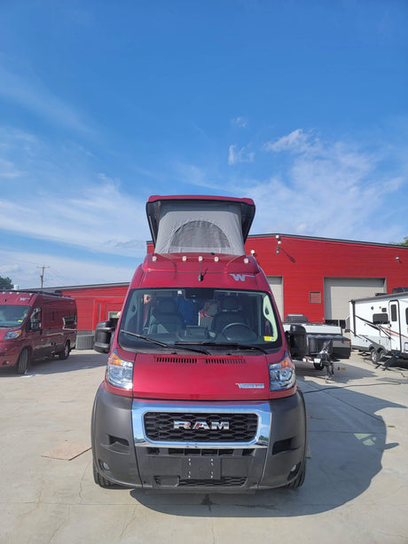 Front view of a red Winnebago Ram camper van with a raised pop-top, ready for rv rental on a sunny day.