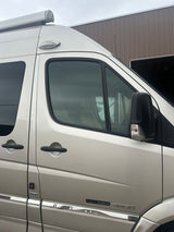 Exterior side view of a light silver Roadtrek camper van with an awning and side mirror, perfect for an RV rental trip.