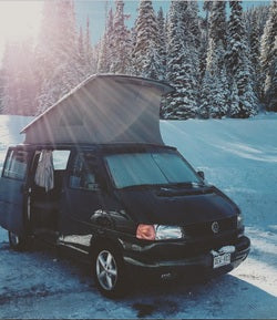 Brightly lit black pop-top VW camper van in snowy forest, perfect for your next RV rental adventure.