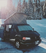 Brightly lit black pop-top VW camper van in snowy forest, perfect for your next RV rental adventure.