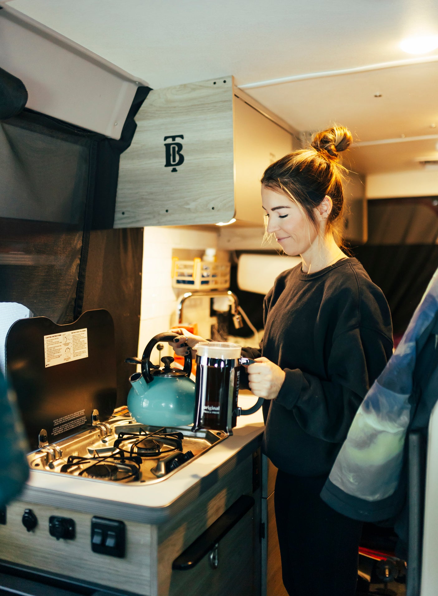 Enjoying morning coffee in an RV rental. A woman uses a French press and kettle in the compact kitchen.