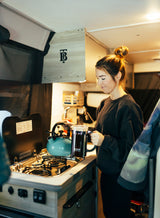 Enjoying morning coffee in an RV rental. A woman uses a French press and kettle in the compact kitchen.