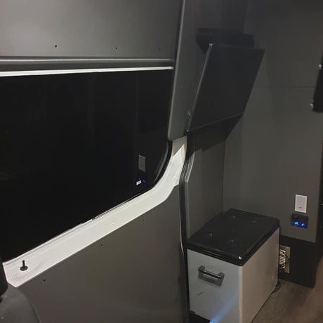 RV rental van conversion: Dark gray interior with large window, portable fridge, power outlets, and open overhead storage.