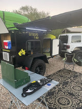 RV rental setup with a black Outbound T-Rex teardrop trailer, kayak, Jeep, and camping gear on a rug.