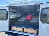Woman relaxing inside an RV rental truck camper, showing the cozy bed and storage for camping adventures.