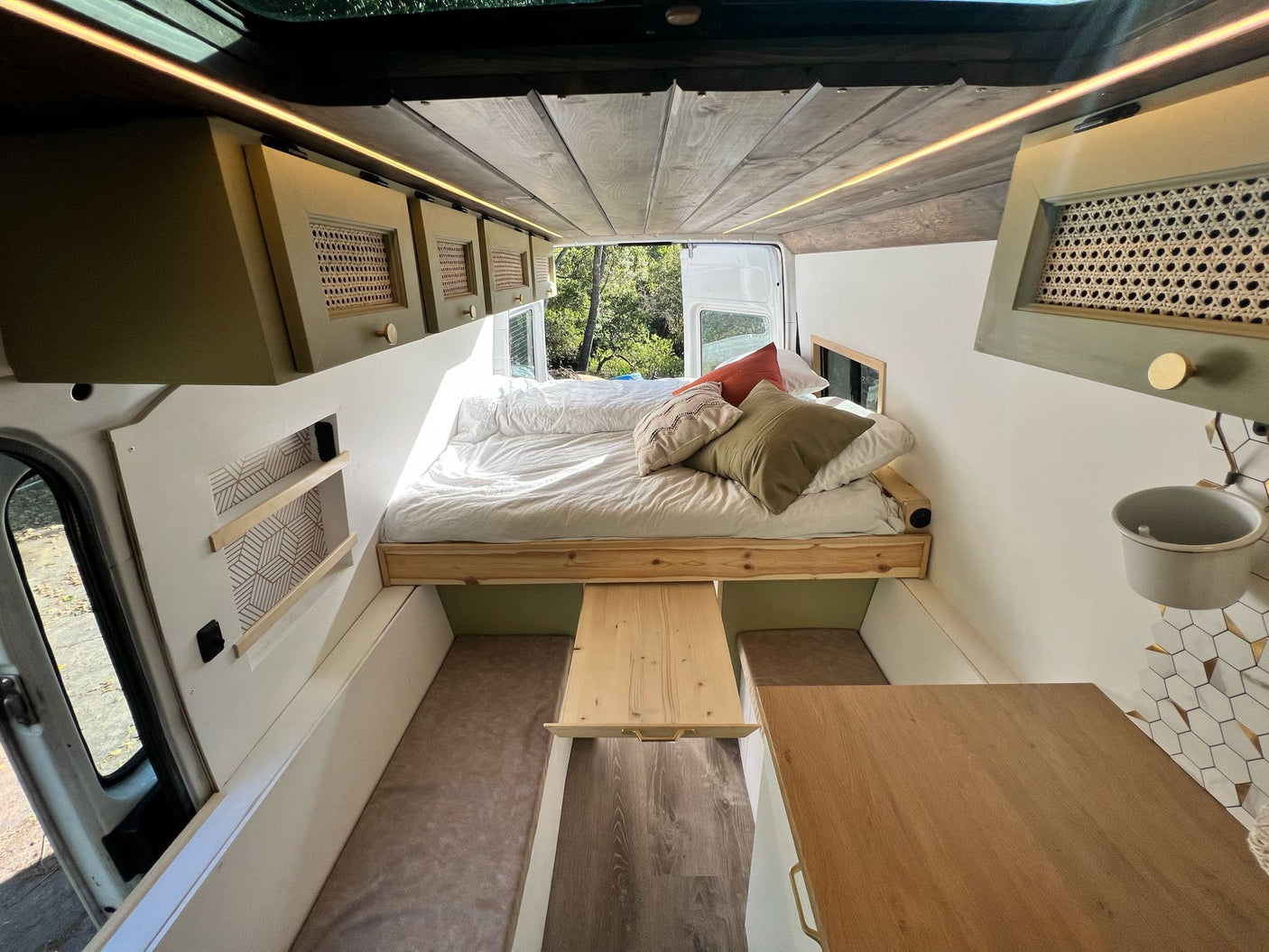 Cozy RV rental interior featuring a raised bed, wooden ceiling, and a practical pull-out table. Ideal for van life travel.