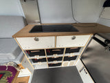 RV rental interior featuring a cooktop, custom labeled storage bins (Sports, Breads, Supplements), and a cozy seating area.