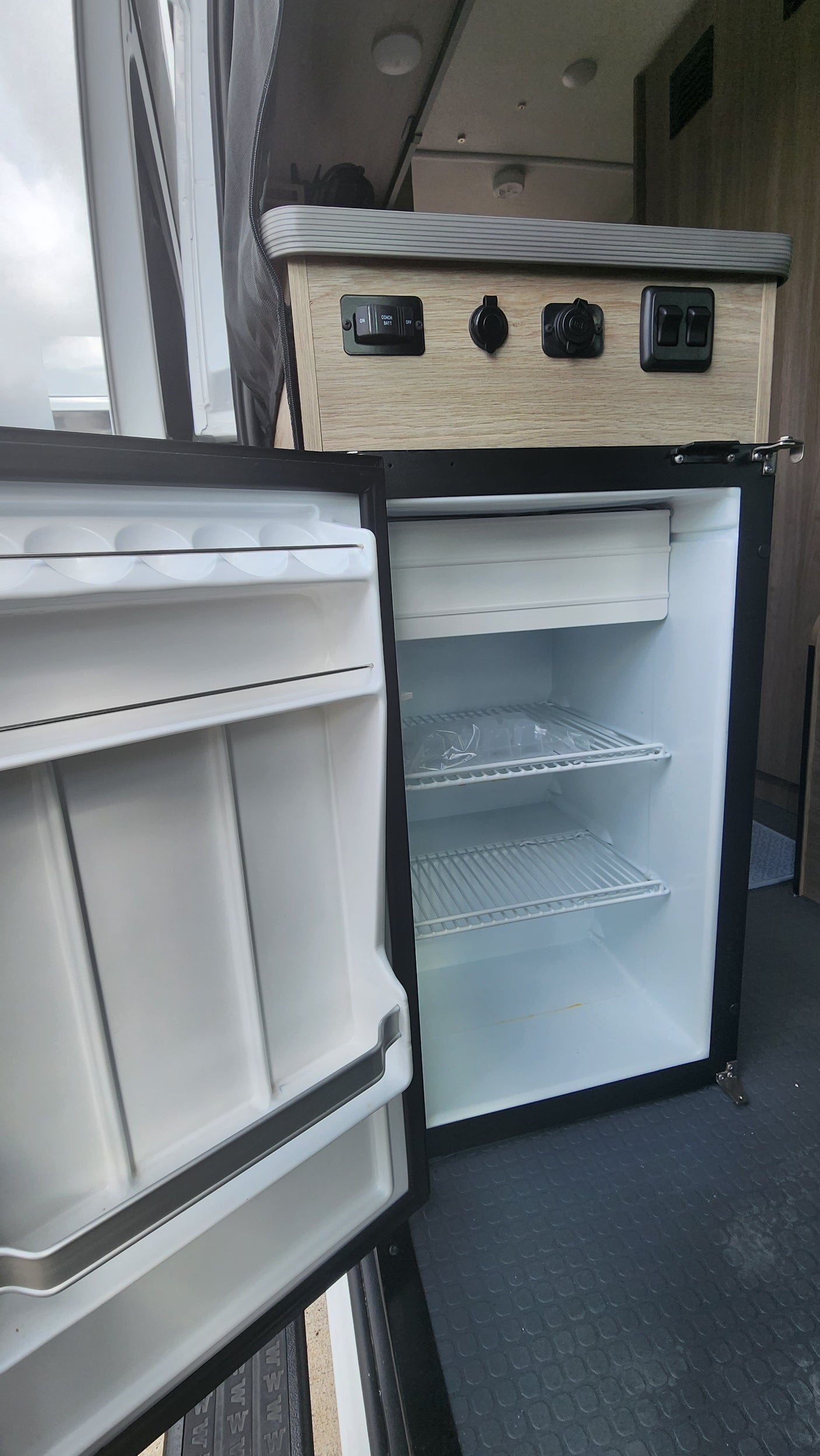 RV rental interior: compact fridge, control panel with switches/outlets. Ideal for mobile living and van life adventures.