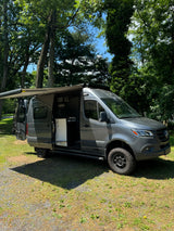 This rugged gray Mercedes-Benz Sprinter campervan rv rental is parked with its awning extended and side door open, ready for adventure.