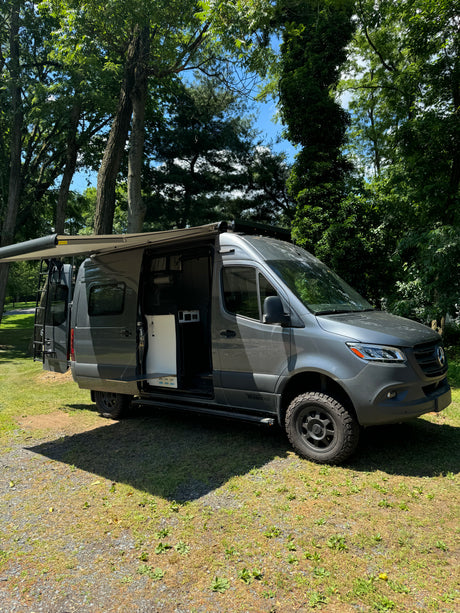 This rugged gray Mercedes-Benz Sprinter campervan rv rental is parked with its awning extended and side door open, ready for adventure.
