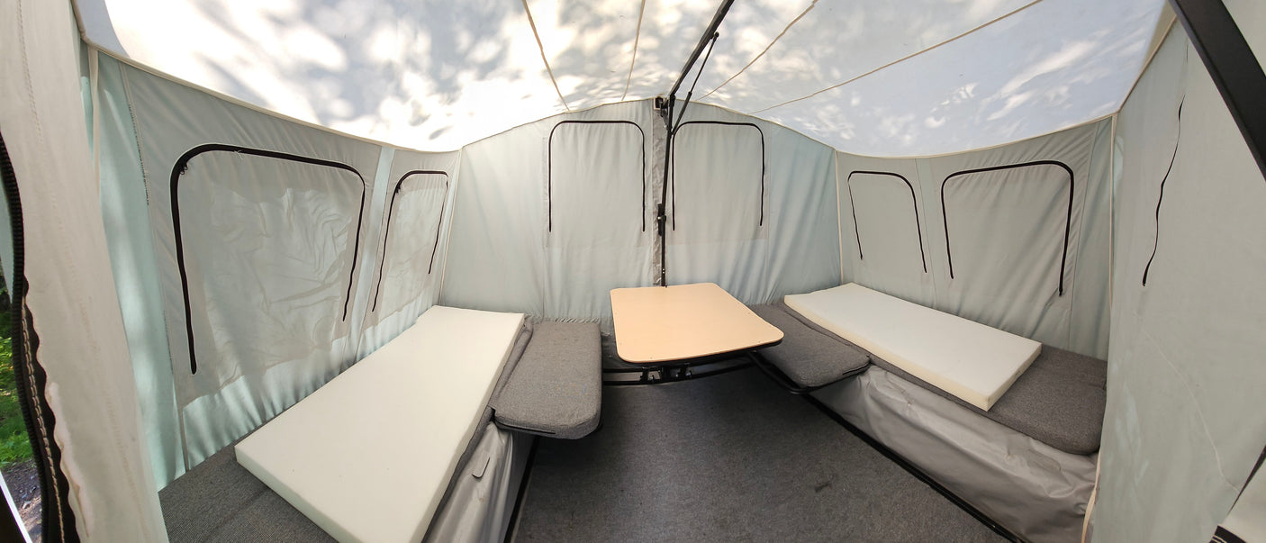 This RV rental's pop-up camper interior features bench beds, a center table, and light tent-style walls.