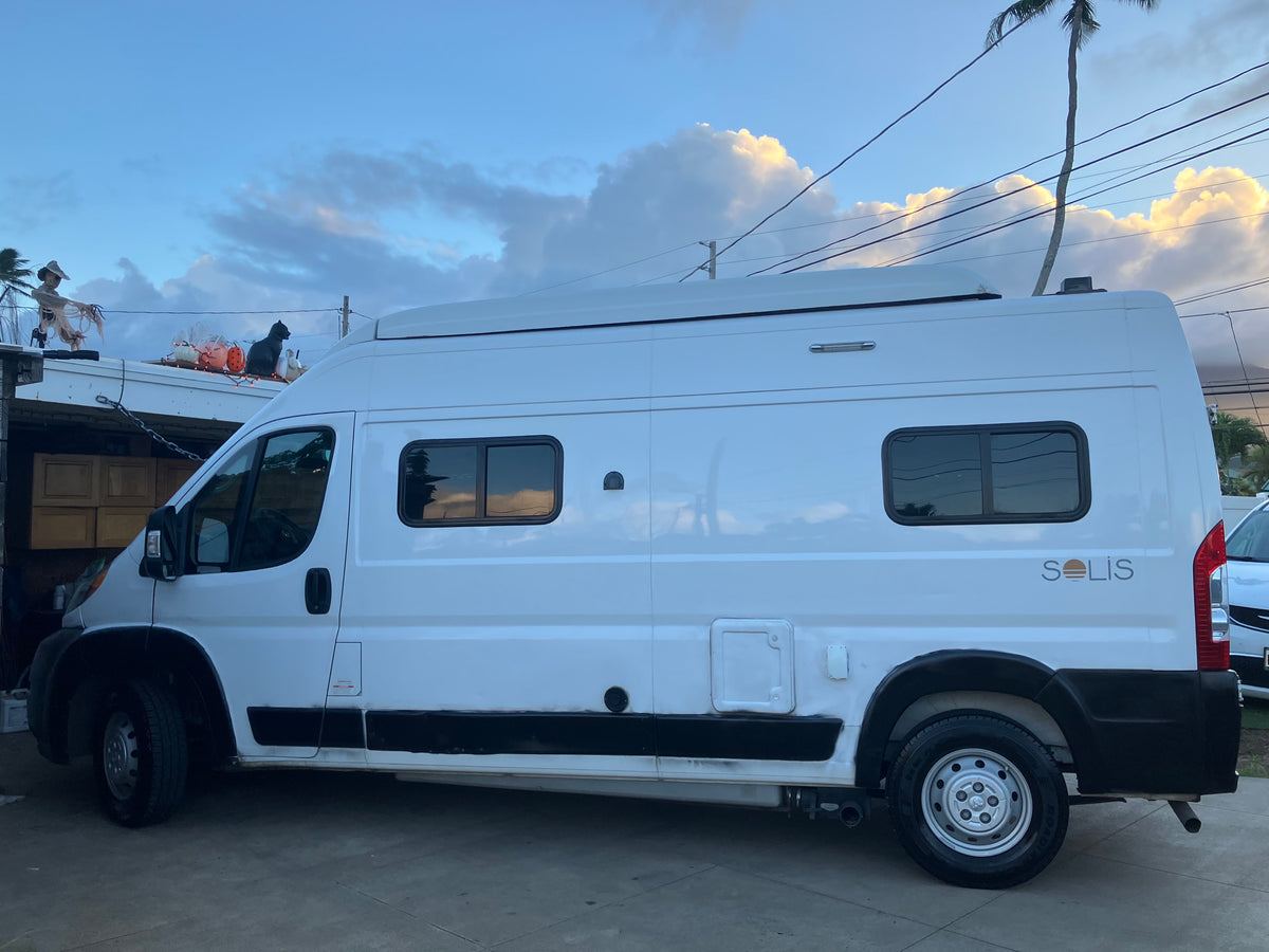 White Winnebago Solis RV rental parked under a partly cloudy sky, with Halloween decorations on a nearby roof. — photo 6