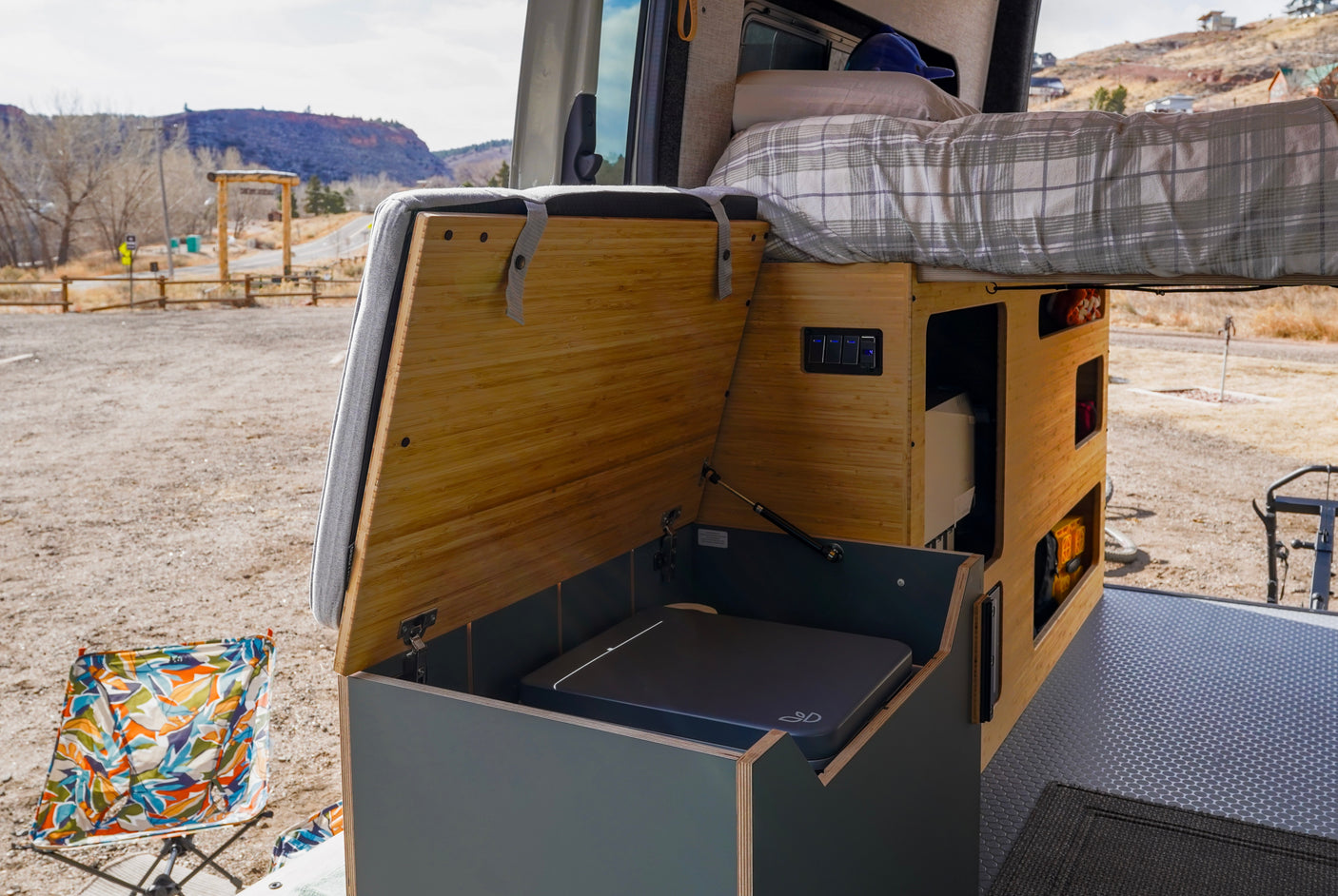 An RV rental camper van interior featuring a cozy bed, bamboo storage, power panel, and Dometic stove for outdoor trips.