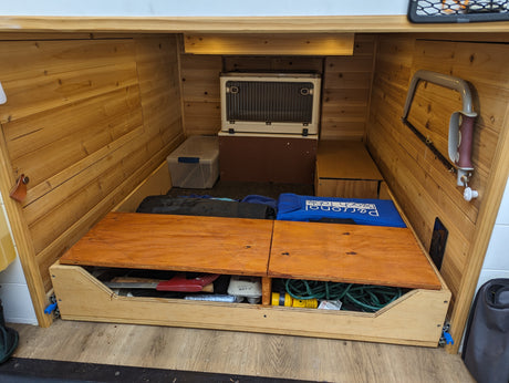 RV rental storage: pull-out drawer, cooler, and tools neatly organized in a wood-paneled space.