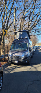 A dark grey Winnebago camper van, a common RV rental choice, parked roadside with pop-top open on a clear day.