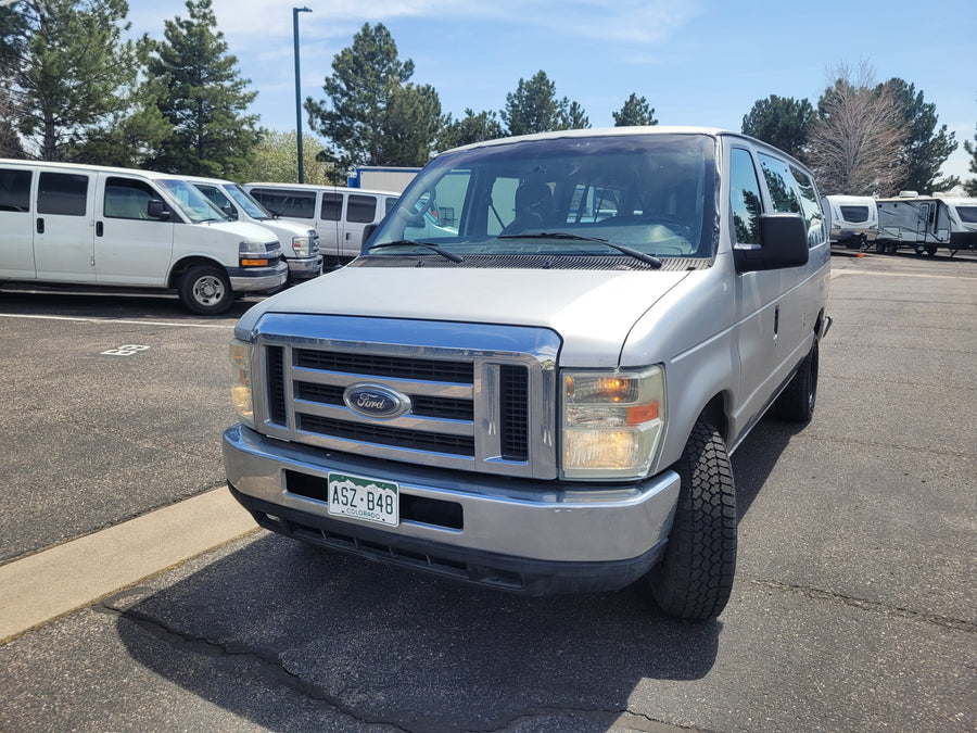 Silver Colorado Ford van at an RV rental lot, with other vans and RVs visible in the background.