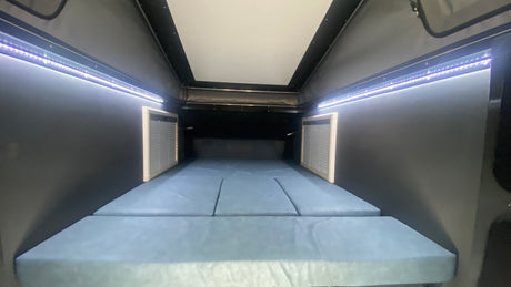 Cozy rv rental interior: A comfortable sleeping area with blue cushion bed & bright LED strip lights along the ceiling.
