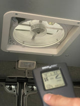 Inside an RV rental, a person checks the MaxxAir ceiling fan and its remote showing 78°F and 93% humidity for ventilation.
