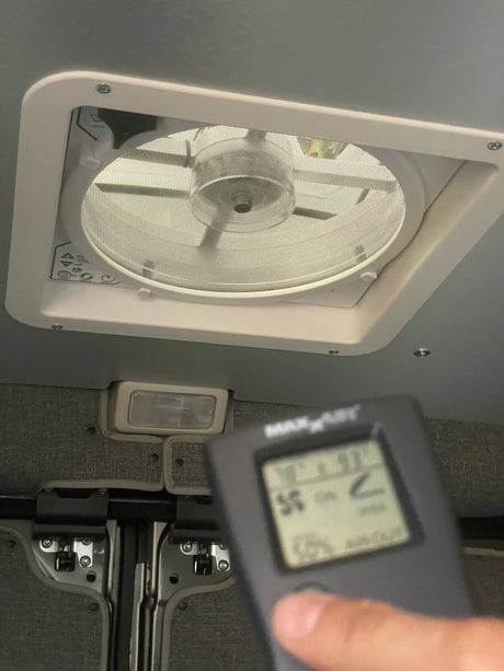 Inside an RV rental, a person checks the MaxxAir ceiling fan and its remote showing 78°F and 93% humidity for ventilation.