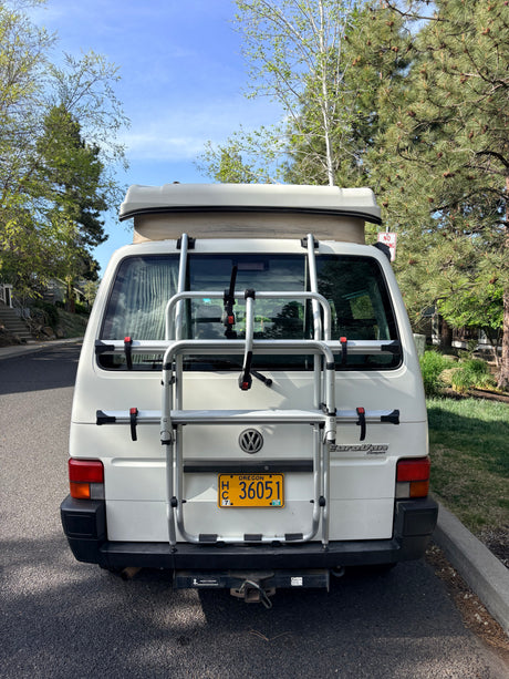 Rear view of a white VW EuroVan camper, an ideal RV rental, with a bike rack & Oregon plate. Parked outside on a sunny day.