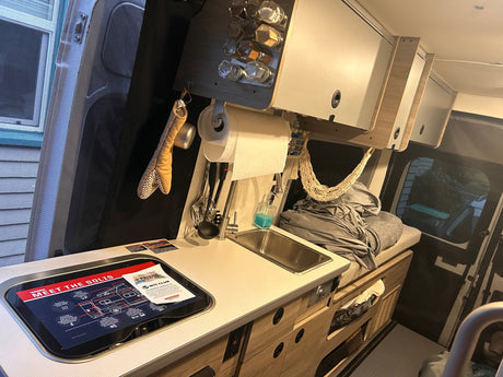 Inside an RV rental, a Winnebago Solis camper van kitchen with sink, stovetop, and overhead storage for compact travel.