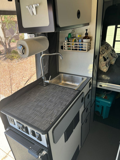 RV rental interior: galley kitchen with sink, paper towels, storage, and controls, featuring a Nova Kool fridge below.