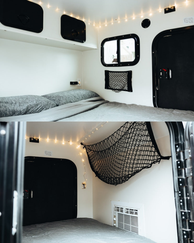 Cozy RV rental interior: a bed with gray bedding, string lights, windows, and storage nets create a warm, functional space.