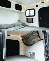 Cozy RV rental interior: a bed with gray bedding, string lights, windows, and storage nets create a warm, functional space.