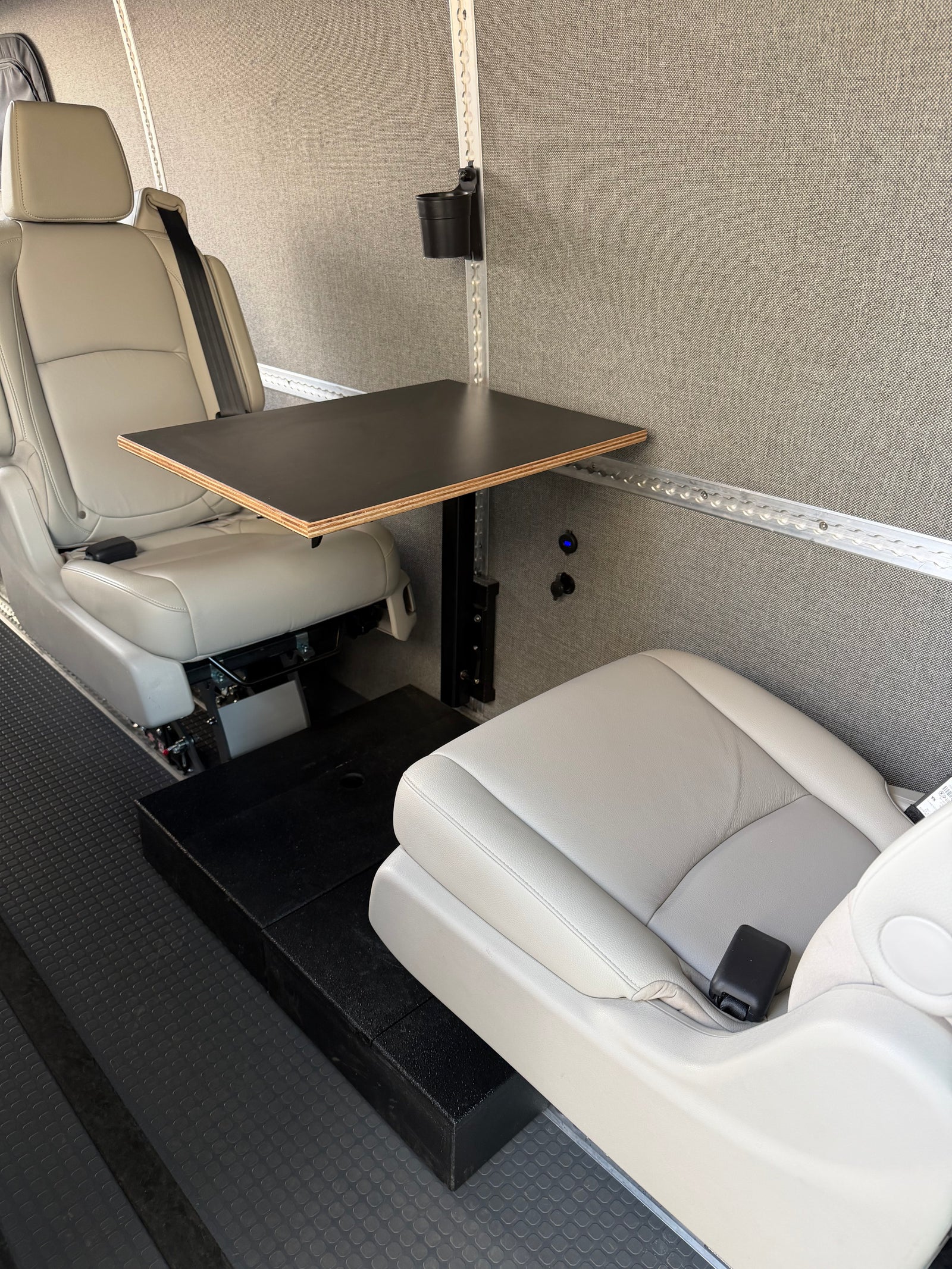 Comfortable RV rental interior with two light gray seats, a small table, and power outlets, ideal for a mobile workspace.