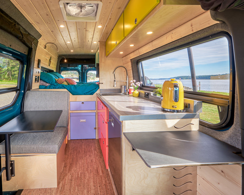 Bright camper van interior: wood walls, vibrant kitchen, cozy bed, dining area, and a large window view of the water, ideal for an RV rental. — photo 2